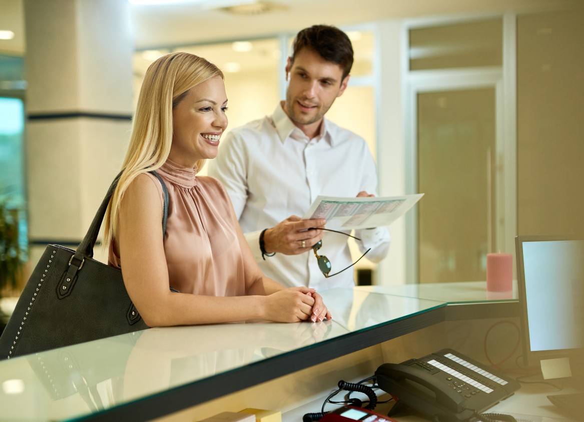 happy-woman-her-husband-standing-reception-desk-while-checking-hotel