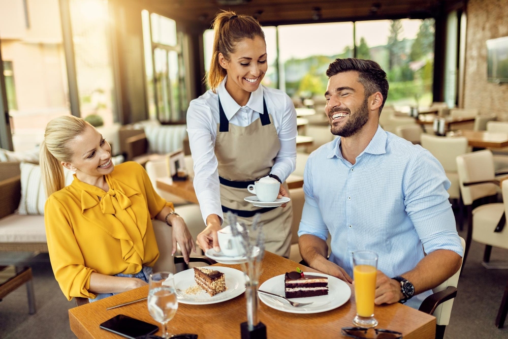 happy-waitress-serving-coffee-couple-who-is-eating-cake-cafe